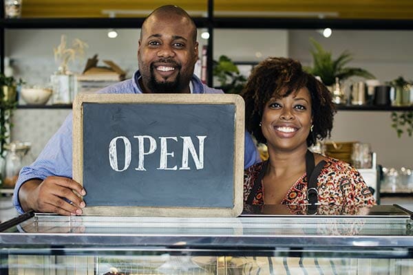 Business Owners smiling in from of OPEN sign