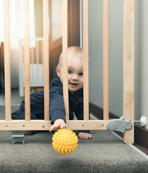 Baby reaching for ball through baby gate